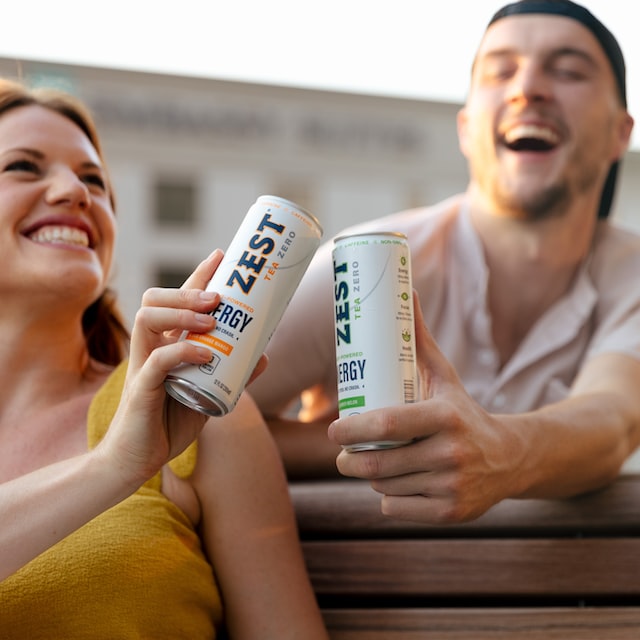 Two people holding onto two canned drinks