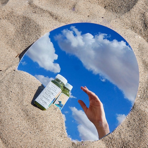 A bottle on a mirror, which is in the sand