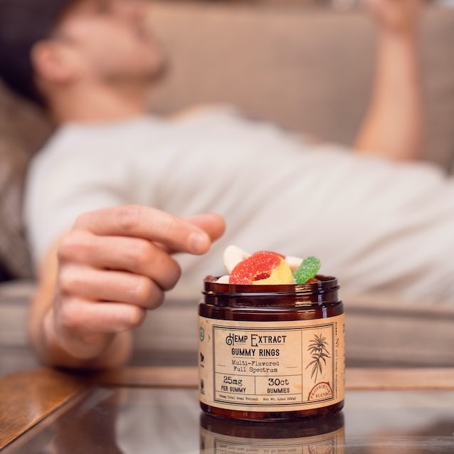 A bottle of gummies with a man in the background reaching for one