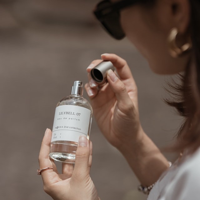 A lady opening the cap of a perfume bottle